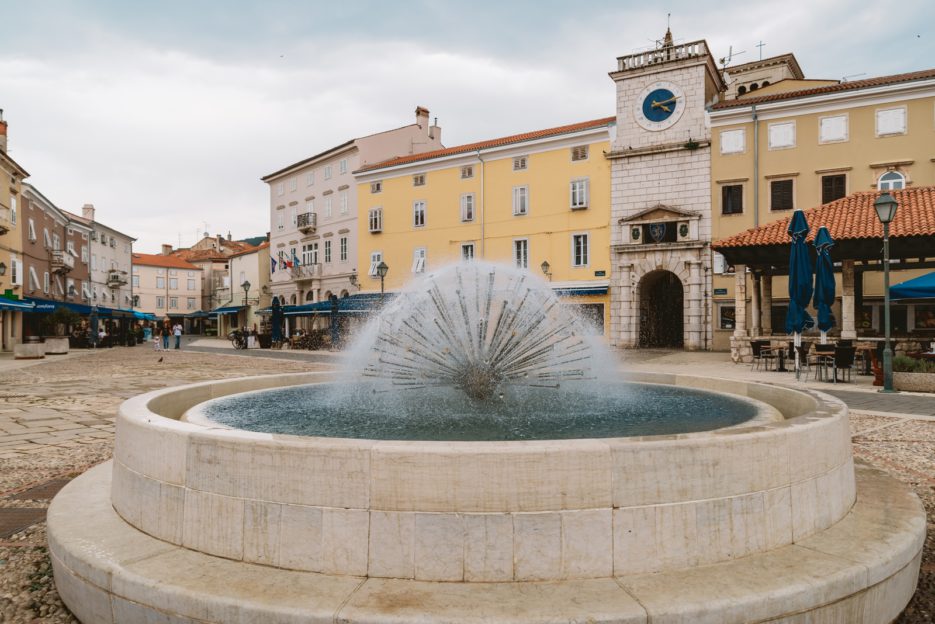 Trg Frane Petrića, główny plac miasta Cres z fontanną Jadran i wieżą zegarową